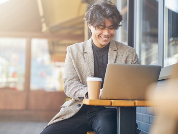 Cheerful young man using laptop in outdoors cafe